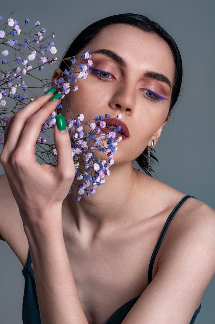 Stylish portrait of a woman with purple eyeshadow holding delicate purple flowers.